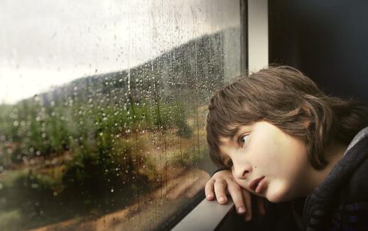 smutny chłopiec patrzy przez okno w czasie deszczu
