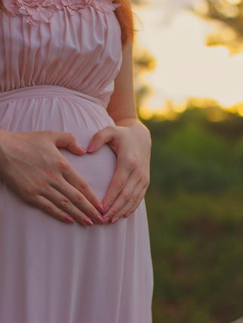 Kobieta w ciąży trzyma dłonie w kształcie serca na brzuchu.